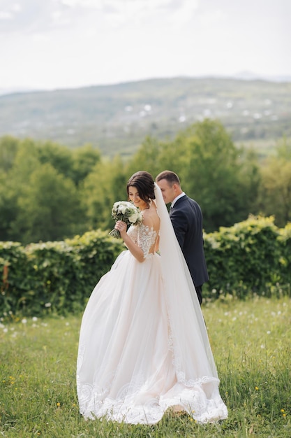 Portrait of the bride and groom in nature A stylish bride and groom in a long lace dress are walking in the garden holding hands Couple in love