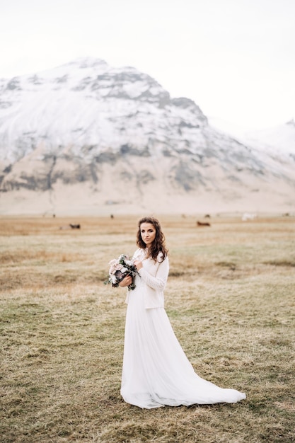 Portrait of a bride in a white wedding dress with a brides bouquet in her hands in a field