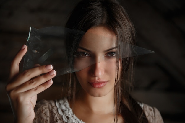 Portrait of a brunette girl looking through a shard of glass