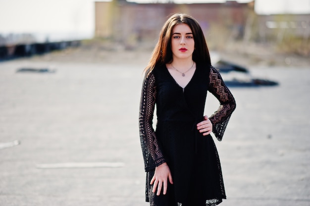 Portrait brunette girl with red lips wearing a black dress posed on the roof