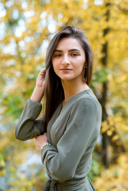 Portrait of brunette woman in green dress posing in autumn park