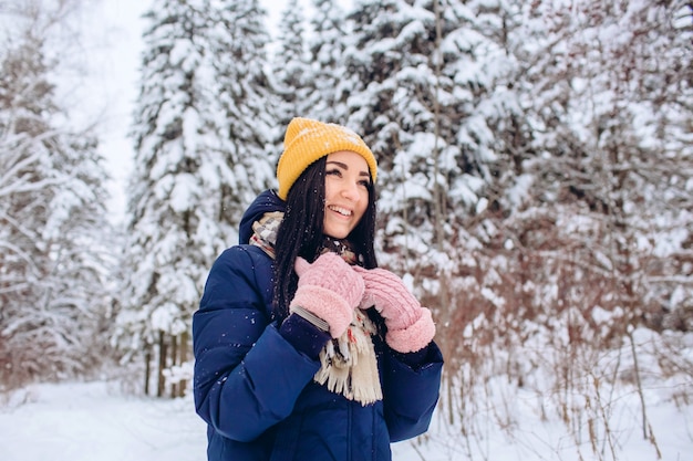 Portrait of a brunette woman in a yellow hat on a background of a winter forest