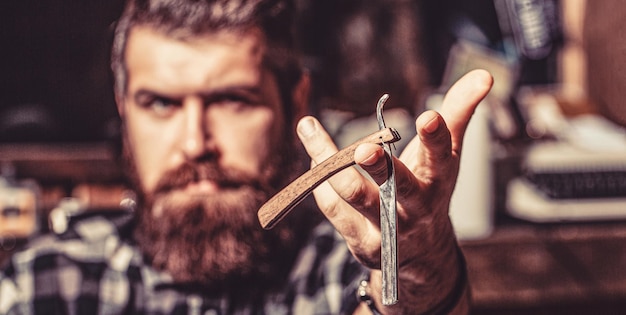 Portrait of brutal bearded man Vintage straight razor Mens haircut Man in barbershop Handsome bearded hairdresser is holding a straight razor while barbershop