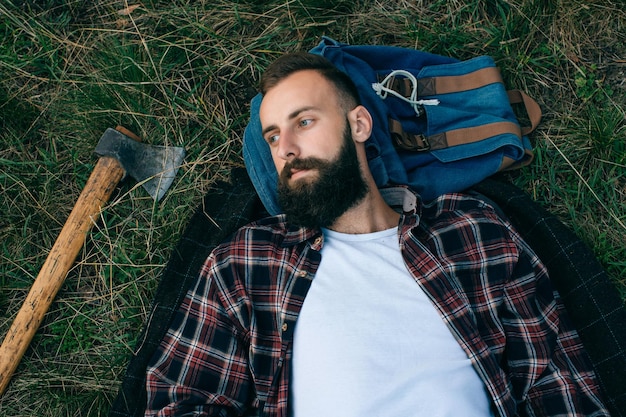 Portrait brutal bearded and moustached woodcutter hipster Gypsy man in the forest with ax Man lying on the grass and dreamsx9