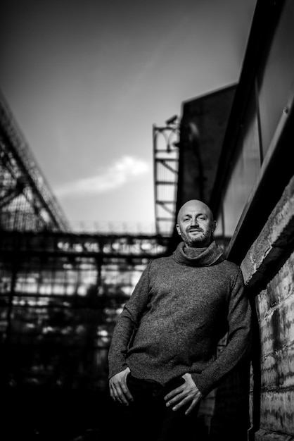 Portrait of a brutal man He stands leaning against a wall his hands in his pockets Stylization for black and white film