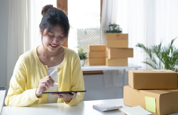 Portrait business Asian woman smile and use tablet checking information on parcel shipping box before send to customer Entrepreneur small business working at home SME business online marketing