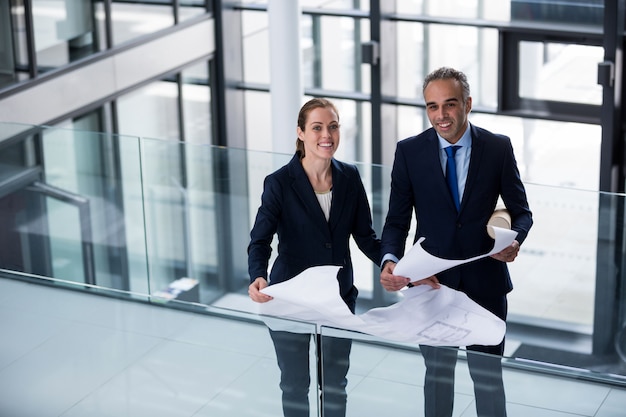 Portrait of business colleagues standing with blueprint in corridor