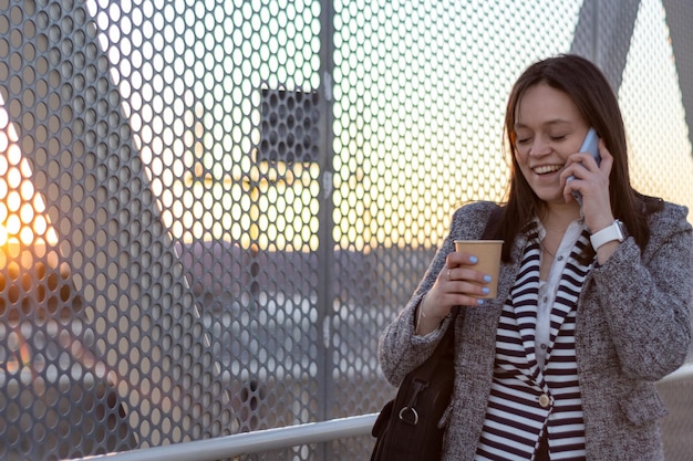 Portrait of a business woman talking on the phone in the street with a coffee in her hand at sunset