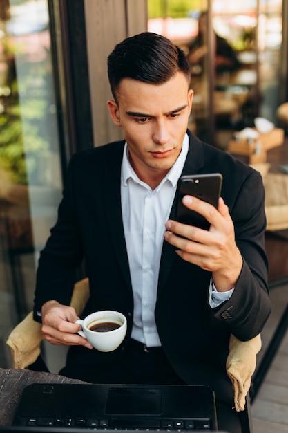 Portrait of businessman  holding a cup of coffe and looking  at the screen of mobile phone