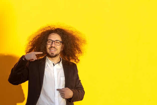 Portrait of businessman man long hair and glasses pointing his teeth and smile over yellow background