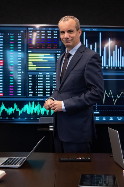 Portrait of businessman posing for camera. Smiling man working in office making financial analysis of stock market data with pleasure, looking at camera. Financial analytics, business strategy concept