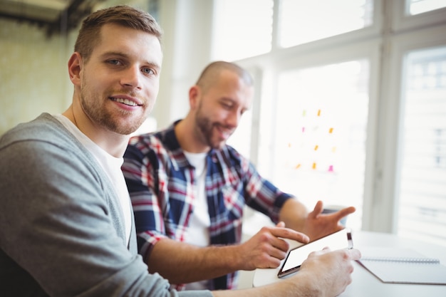 Portrait of businessman with colleague using digital tablet in office