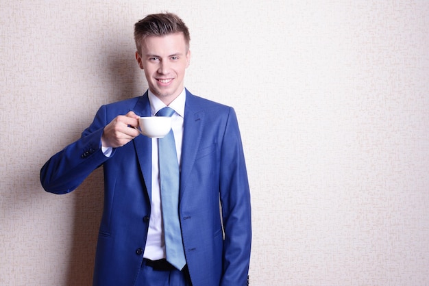 Portrait of businessman with cup of coffee near wall