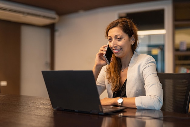 Portrait of businesswoman using laptop computer at night in office while talking on phone