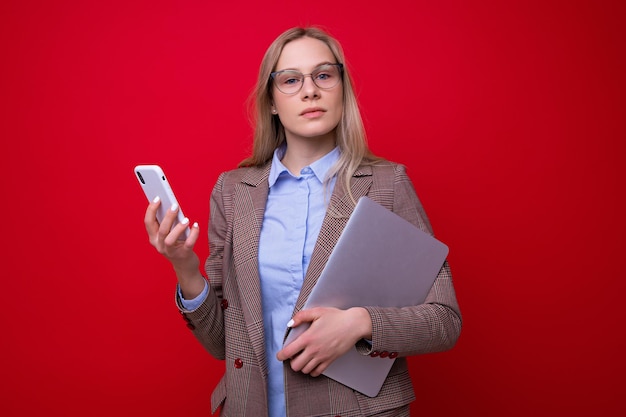 Portrait of a businesswoman with a laptop and phone on a red background