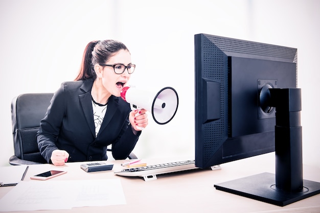 Portrait of a businesswoman yelling through a megaphone sitting in the office