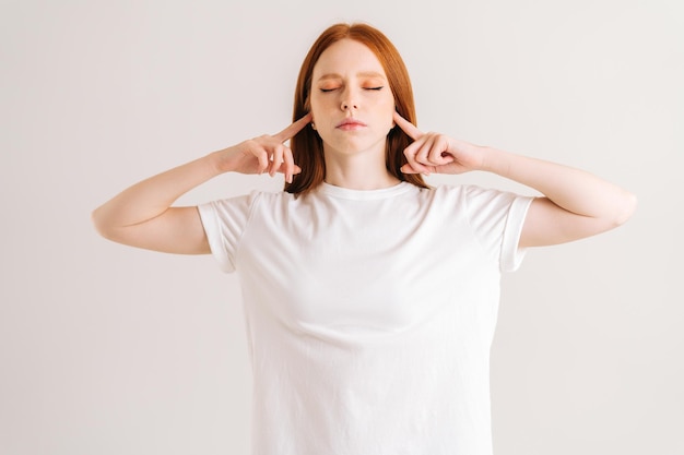 Portrait of calm young woman covering her ears and gesticulating say no blablabla standing on white