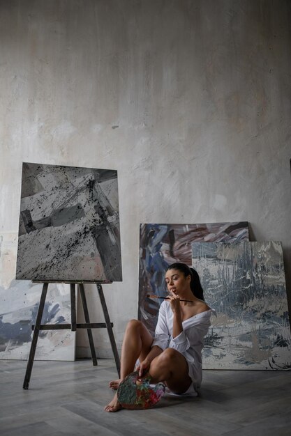 Portrait of candid authentic sexy mixed race girl in white shirt posing against her paintings