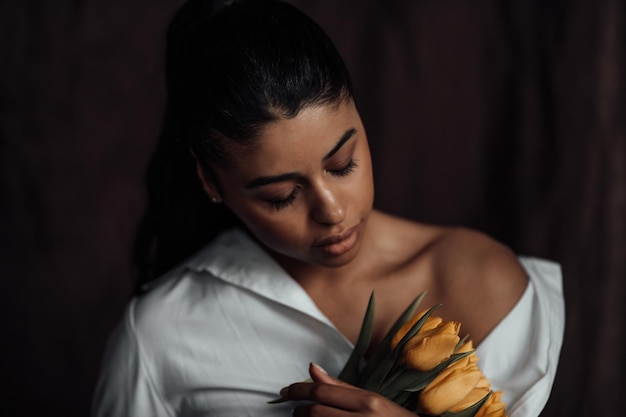 Portrait of candid authentic sexy mixed race girl in white shirt posing hugging bouquet of tulips