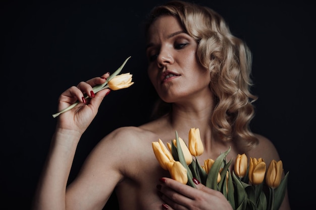 Portrait of candid authentic sexy model blonde girl half naked posing hugging bouquet of tulips