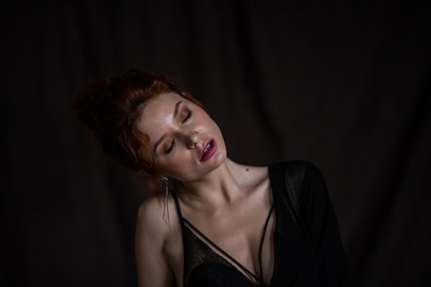 Portrait of candid authentic sexy redhead model girl posing in black blouse with bra at studio