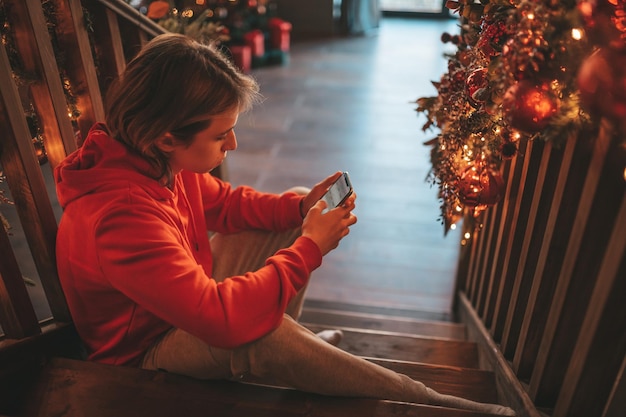 Portrait of candid authentic smiling handsome boy teenager using mobile phone at Xmas home interior