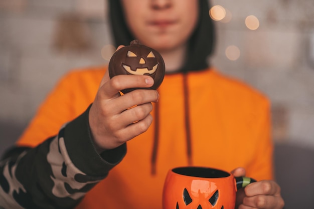 Portrait of candid authentic zoomer boy posing with cup of tea and sweets at home Halloween party