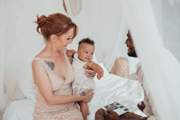 Portrait of candid friendly happy interracial family with swarthy baby together at cozy bedroom