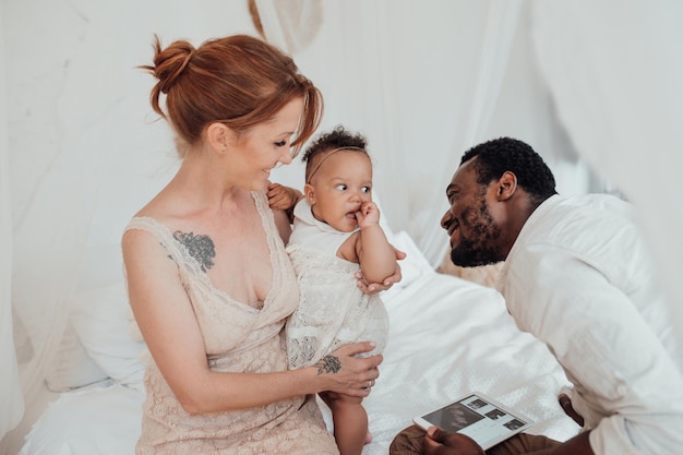 Portrait of candid friendly happy interracial family with swarthy baby together at cozy bedroom