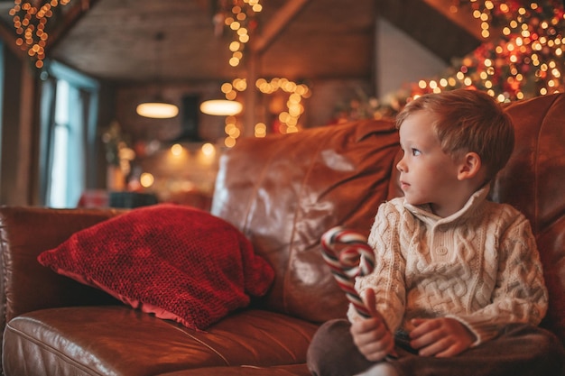 Portrait candid happy kid in knit beige sweater hold Xmas mug with marshmallows and candy cane