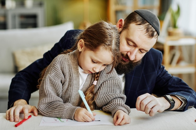 Portrait of caring jewish father drawing pictures with daughter at home