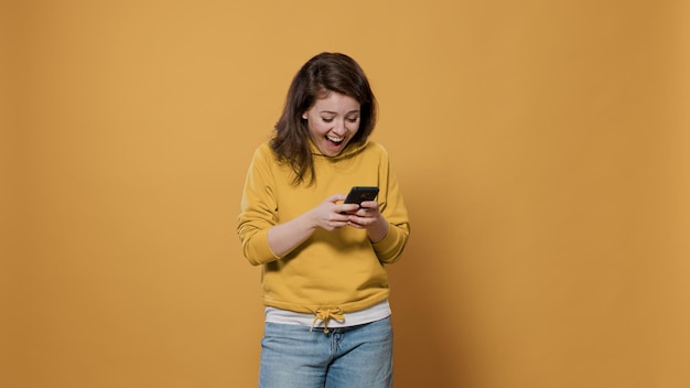 Portrait of casual woman holding smartphone texting having funny online conversation on social media messaging app in studio. Laughing person in her late 20s using digital touchscreen device.