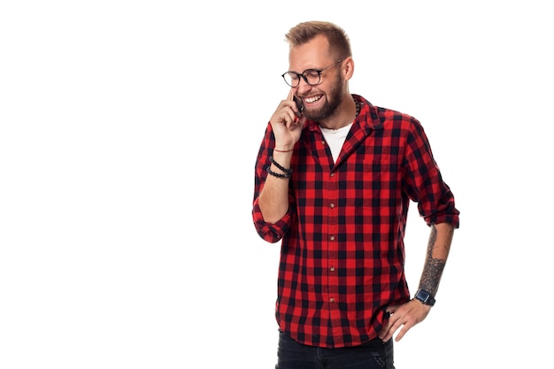 Portrait of a casual young man speaking on the phone and smiling while looking away, somewhere up. Studio shot. Young hipster man in checkered shirt and glasses wearing on white background