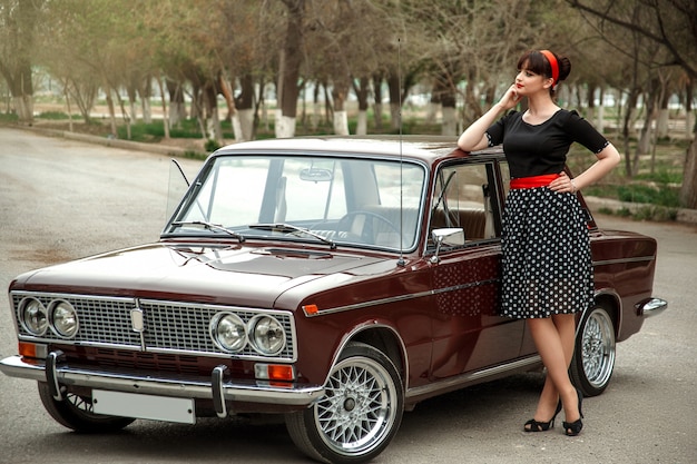 Portrait of a Caucasian beautiful young girl in a black vintage dress, posing near a vintage car 