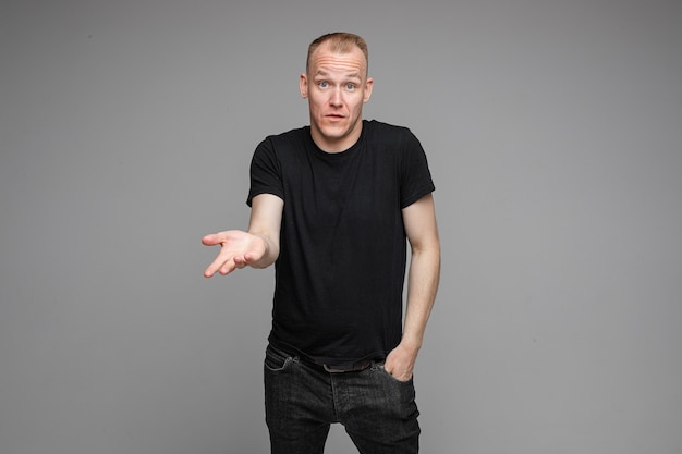 Portrait of Caucasian blond man in black clothing showing disbelief shrugging his shoulders and pointing at camera with his hand asking what is the problem.