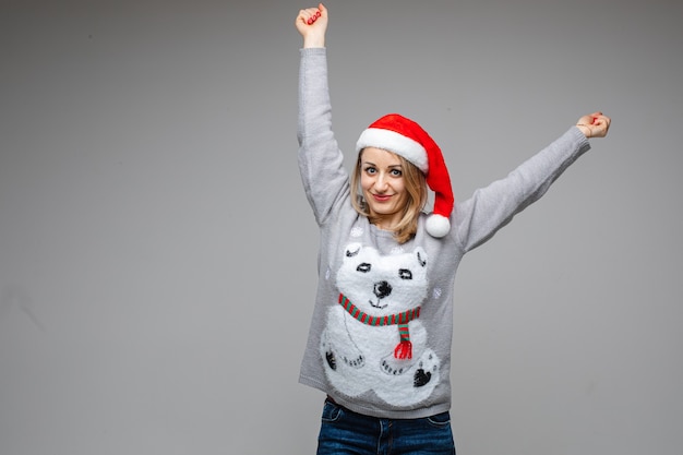 Portrait of Caucasian blonde woman in red Santa hat and winter sweater with polar bear outstretching her arms