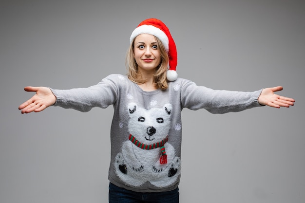 Portrait of Caucasian blonde woman in red Santa hat and winter sweater with polar bear outstretching her arms