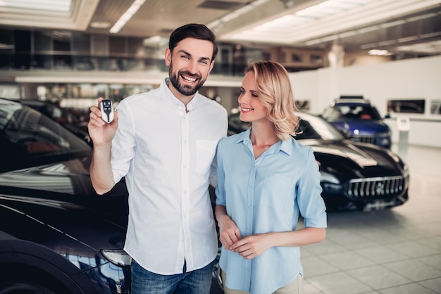 Portrait of caucasian couple holding keys of new car in dealership salon