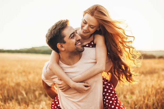 Portrait of a caucasian couple man carrying on back redhead lover anjoying sunlight weekend vacation...