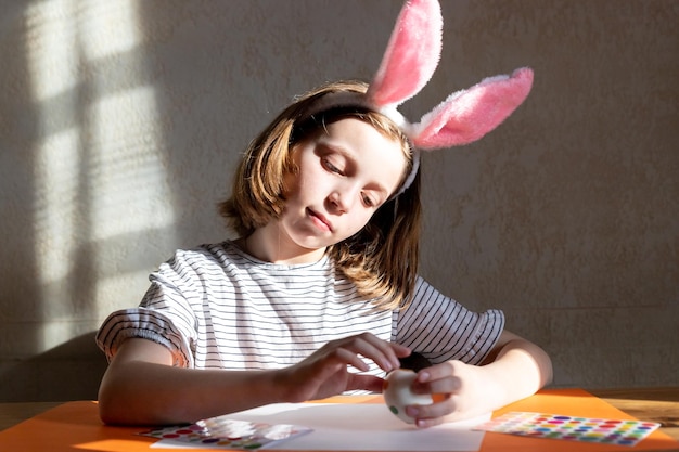 Portrait of caucasian girl decorating easter eggs in the domestic kitchenholidays family and people conceptlittle girl with bunny ears making Easter decoration