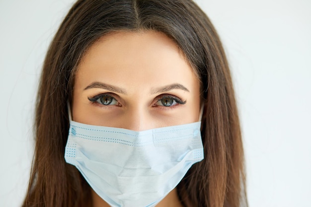 Portrait of Caucasian goodlooking woman doctor in medical mask looking at camera Close up of female physician in respiratory protection