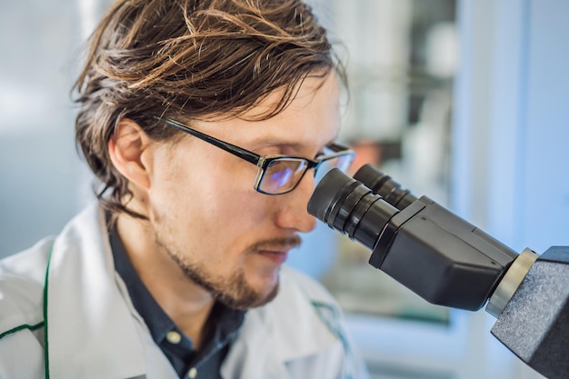 Portrait of caucasian male chemist scientific researcher using microscope in the laboratory interior