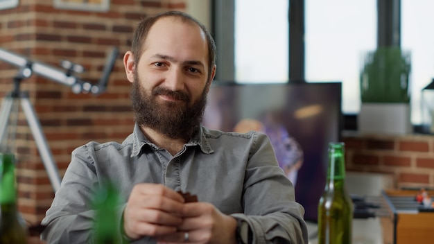 Portrait of caucasian man drinking beer and playing cards game, having fun with cheerful friends. Male person enjying board games and serving alcoholic drinks at table. Close up.