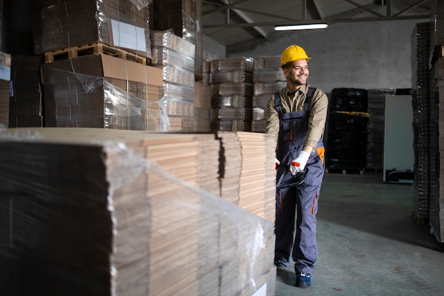 Portrait of caucasian smiling warehouse worker pulling load and palettes on manual forklift in storage room.