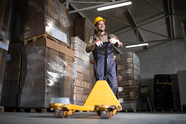 Portrait of caucasian smiling warehouse worker standing by manual forklift in storage room.