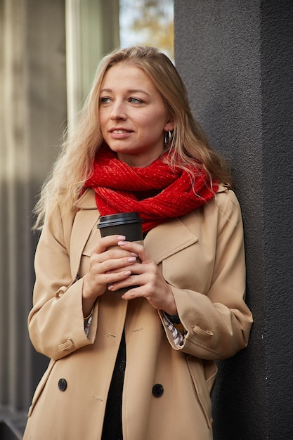 Portrait of caucasian woman in beige trench coat outdoors with cup of coffee