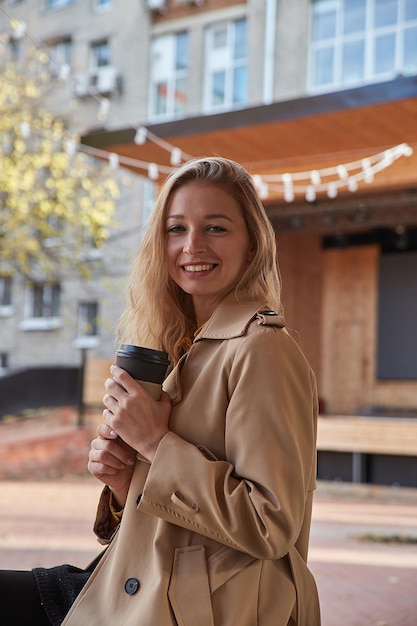 Portrait of caucasian woman in beige trench coat outdoors with cup of coffee