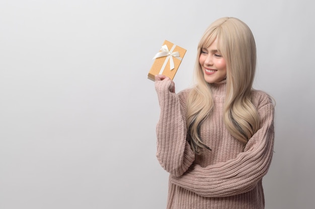 Portrait of Caucasian young woman wearing sweater holding gifts box over white background