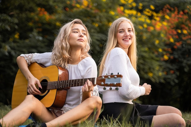 Portrait of caucasian young women sitting in the park outdoor and playing a guitar sing a song together with happiness