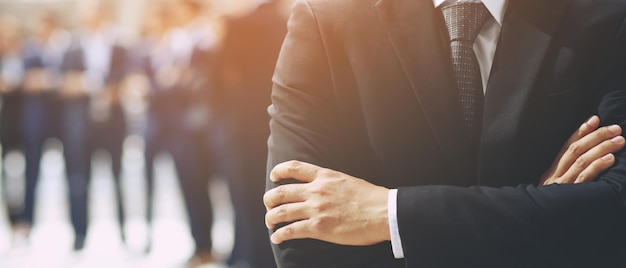 Portrait of a CEO businessman standing hand cross arm successful business team in a classic black suit with employee in background